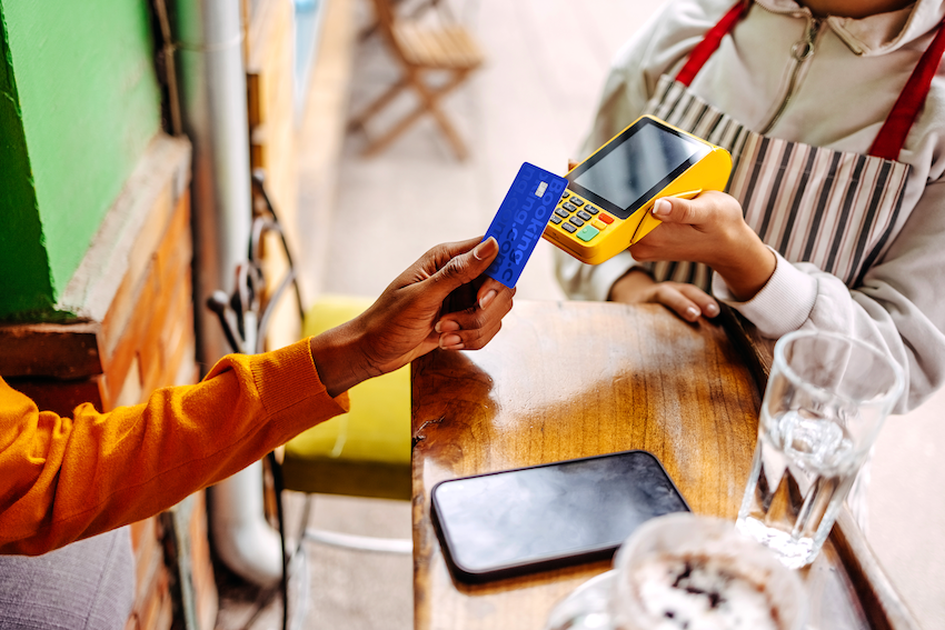 Close-up of a person's hand using a contactless Booking.com card to pay on a modern payment machine.